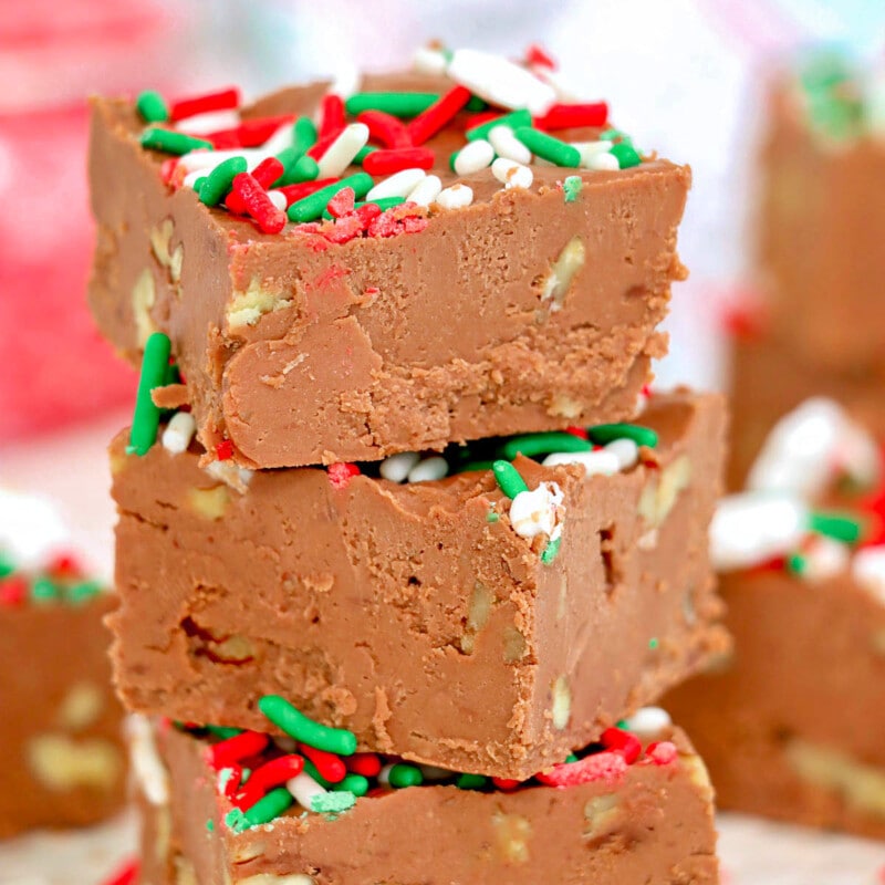 three pieces of chocolate fudge stacked on top of each other. Made with walnuts and topped with red white and green christmas sprinkles.