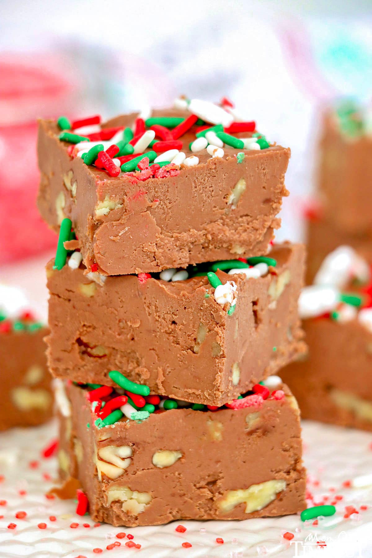 three pieces of chocolate fudge stacked on top of each other. Made with walnuts and topped with red white and green christmas sprinkles.