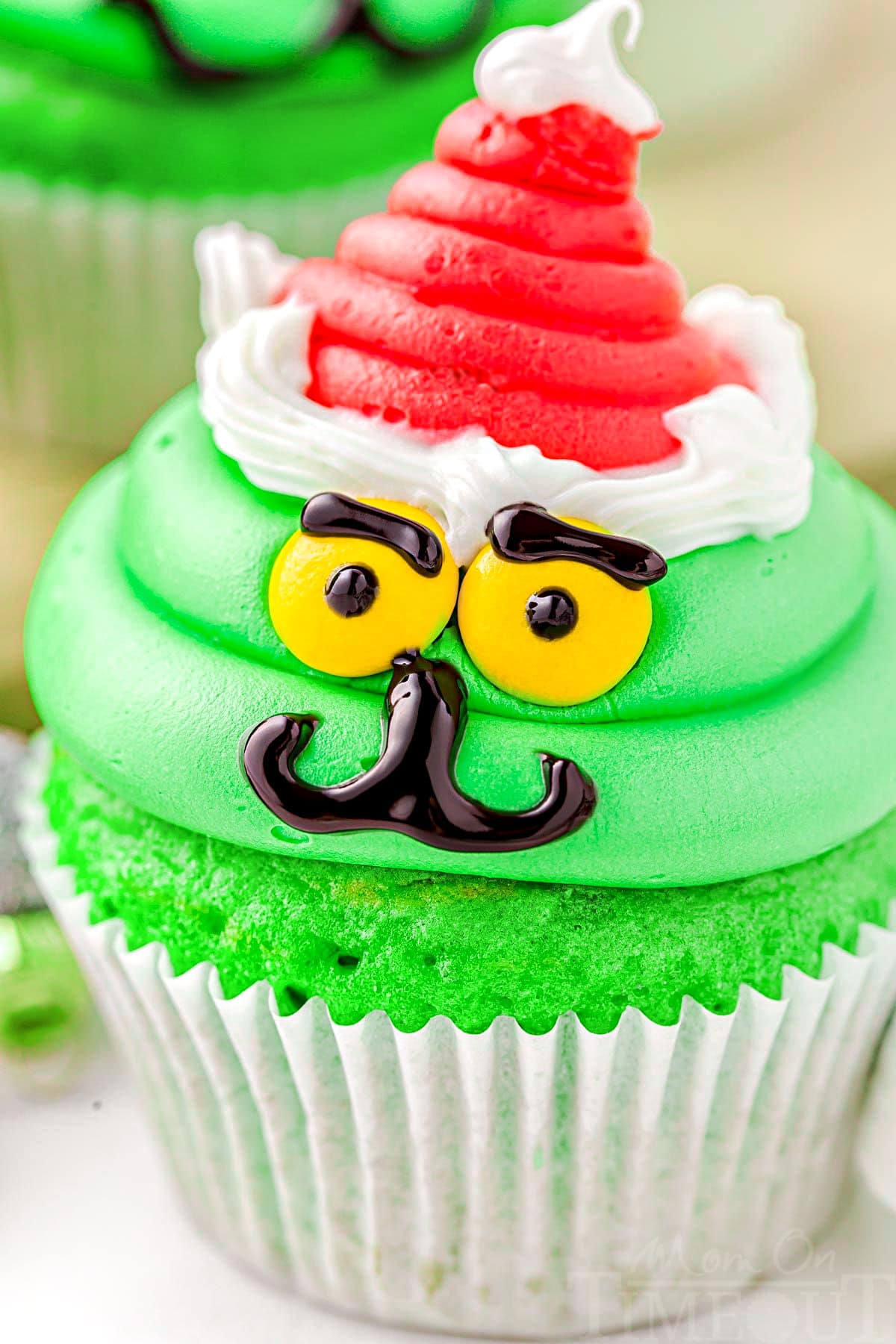 close up look at grinch decorated cupcake complete with santa hat. bright green frosting and cupcake.