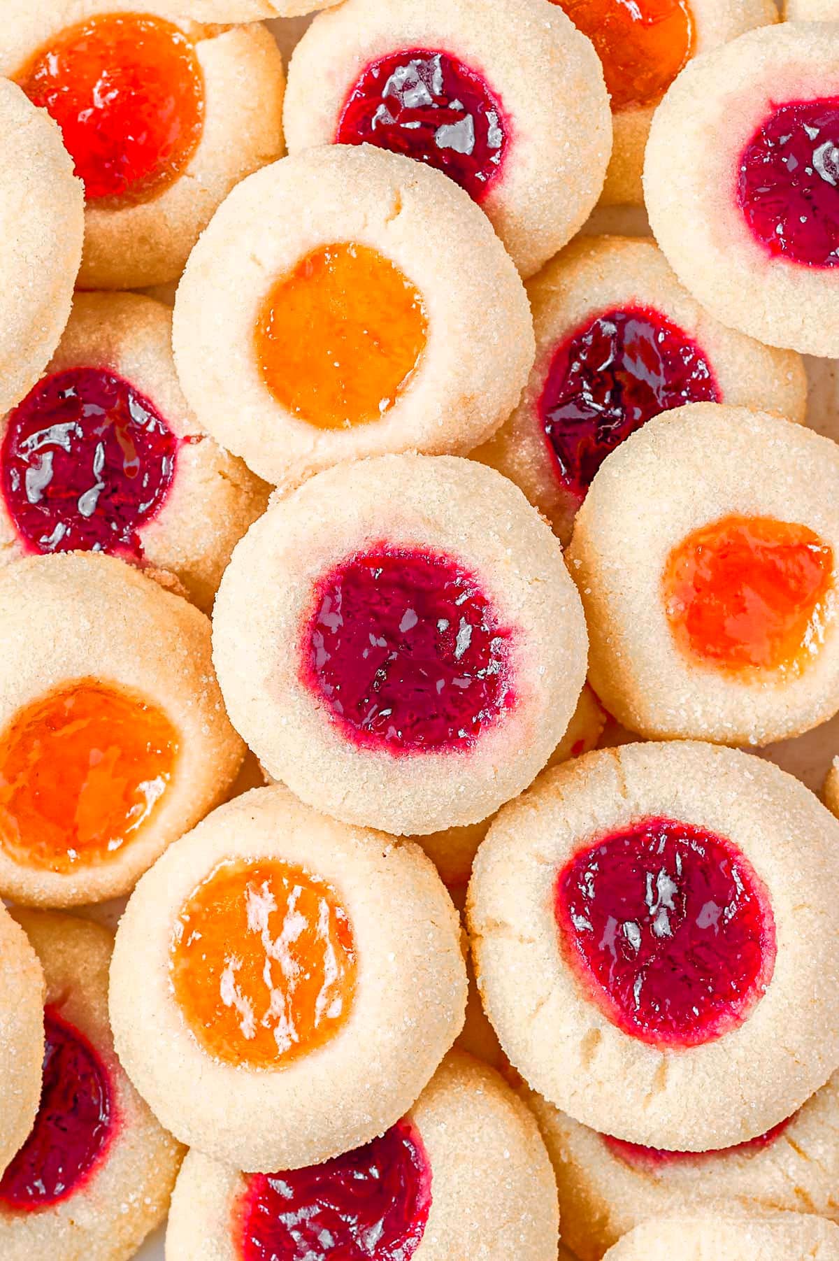 top down look at jam filled cookies piled on a plate with bright orange and red jam filled centers.