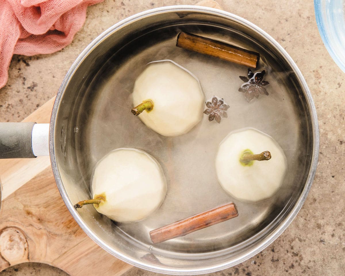 top down shot of three pears being poached in a saucepan.