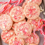 peppermint cookies piled high on a parchment lined baking sheet with candy canes scattered about.