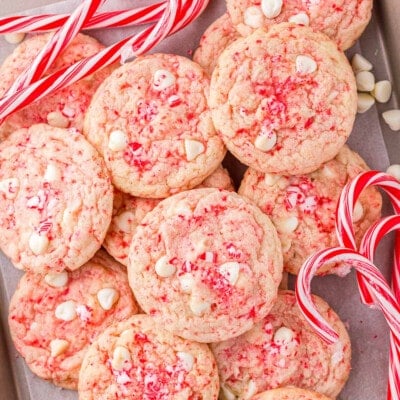 peppermint cookies piled high on a parchment lined baking sheet with candy canes scattered about.