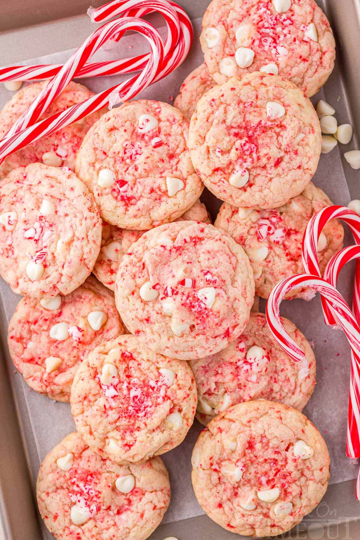 peppermint cookies piled high on a parchment lined baking sheet with candy canes scattered about.