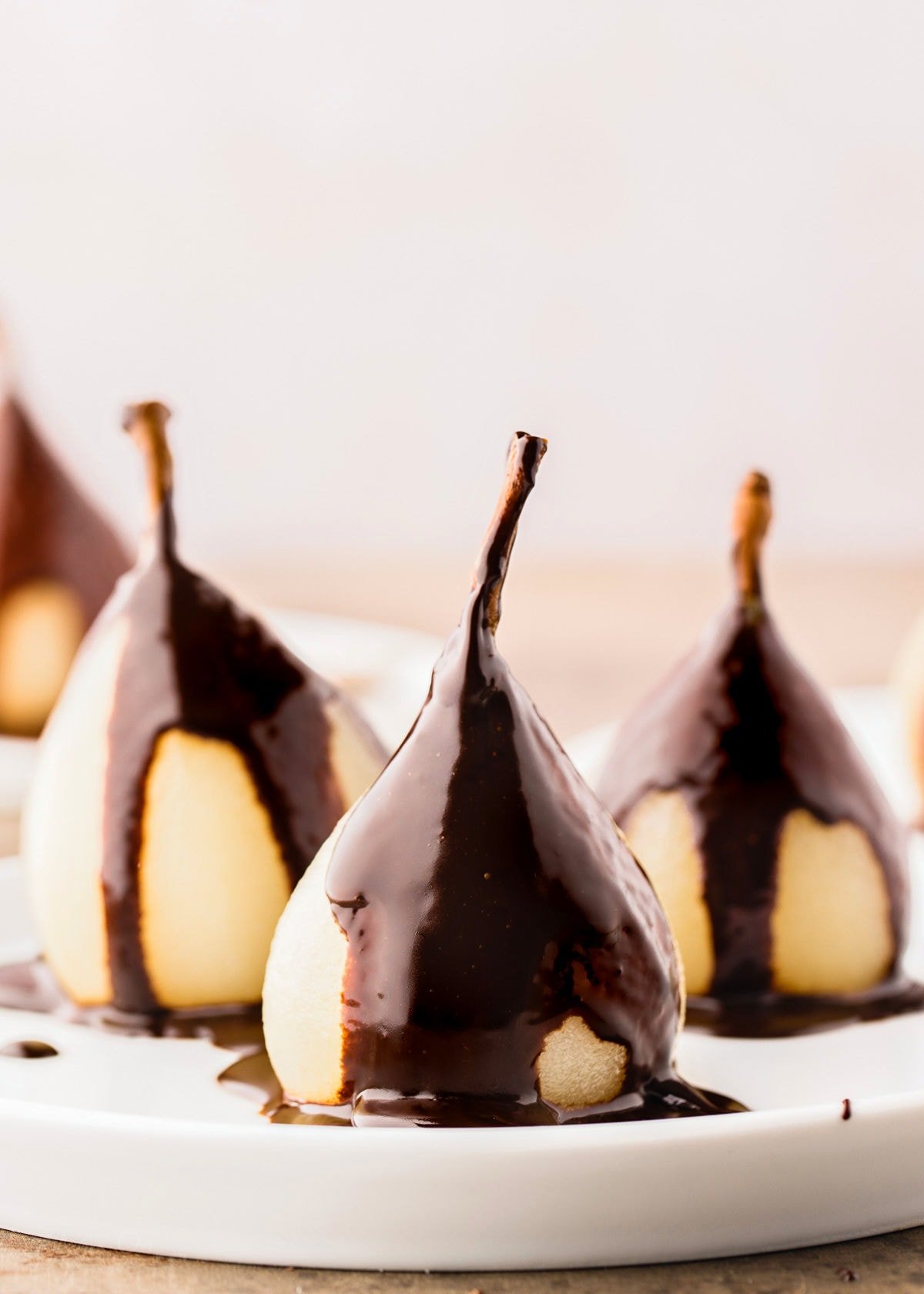 three poached pears on a white plate topped with a creamy chocolate sauce.