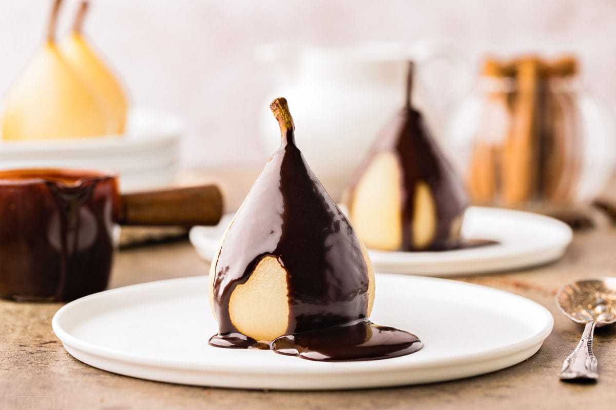 poached pear on a white plate topped with a creamy chocolate sauce.