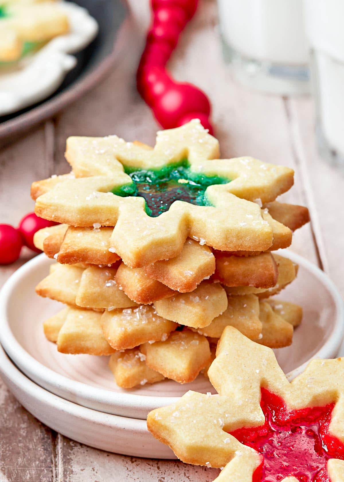 stack of stained glass cookies on a white plate. cookies are snowflake shaped with red and green centers.