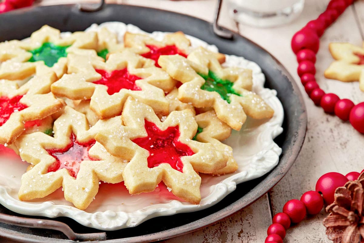 white plate filled with stained glass cookies sitting on a dark metal tray. red beads are sitting next to the plate.