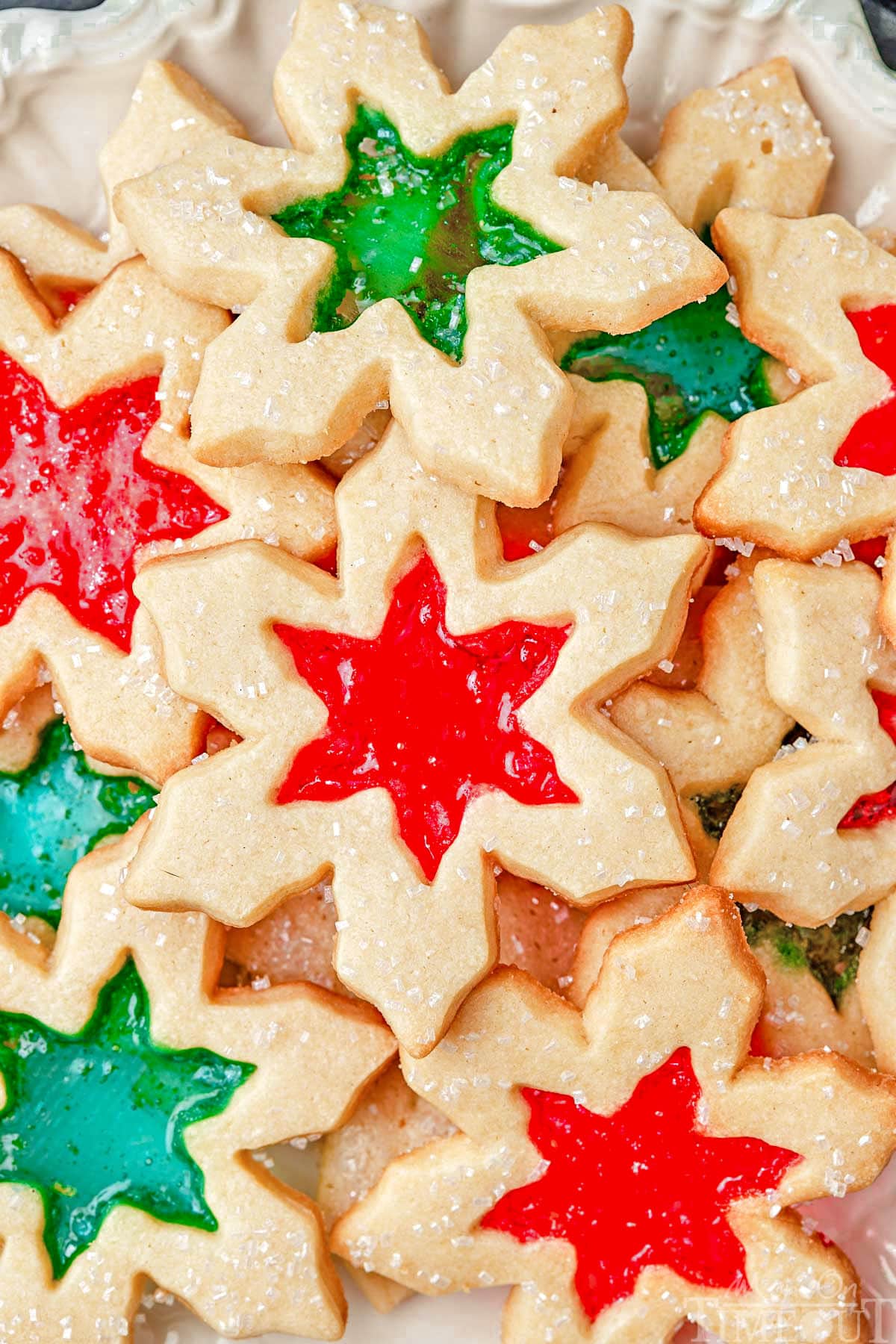 top down look at tray loaded with stained glass cookies with red and green centers cut into snowflake shapes.