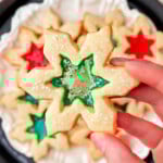 hand holding stained glass cookie over a plate of more cookies. centers are green and red.