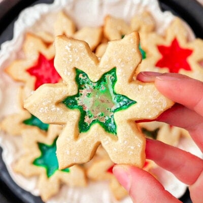 hand holding stained glass cookie over a plate of more cookies. centers are green and red.