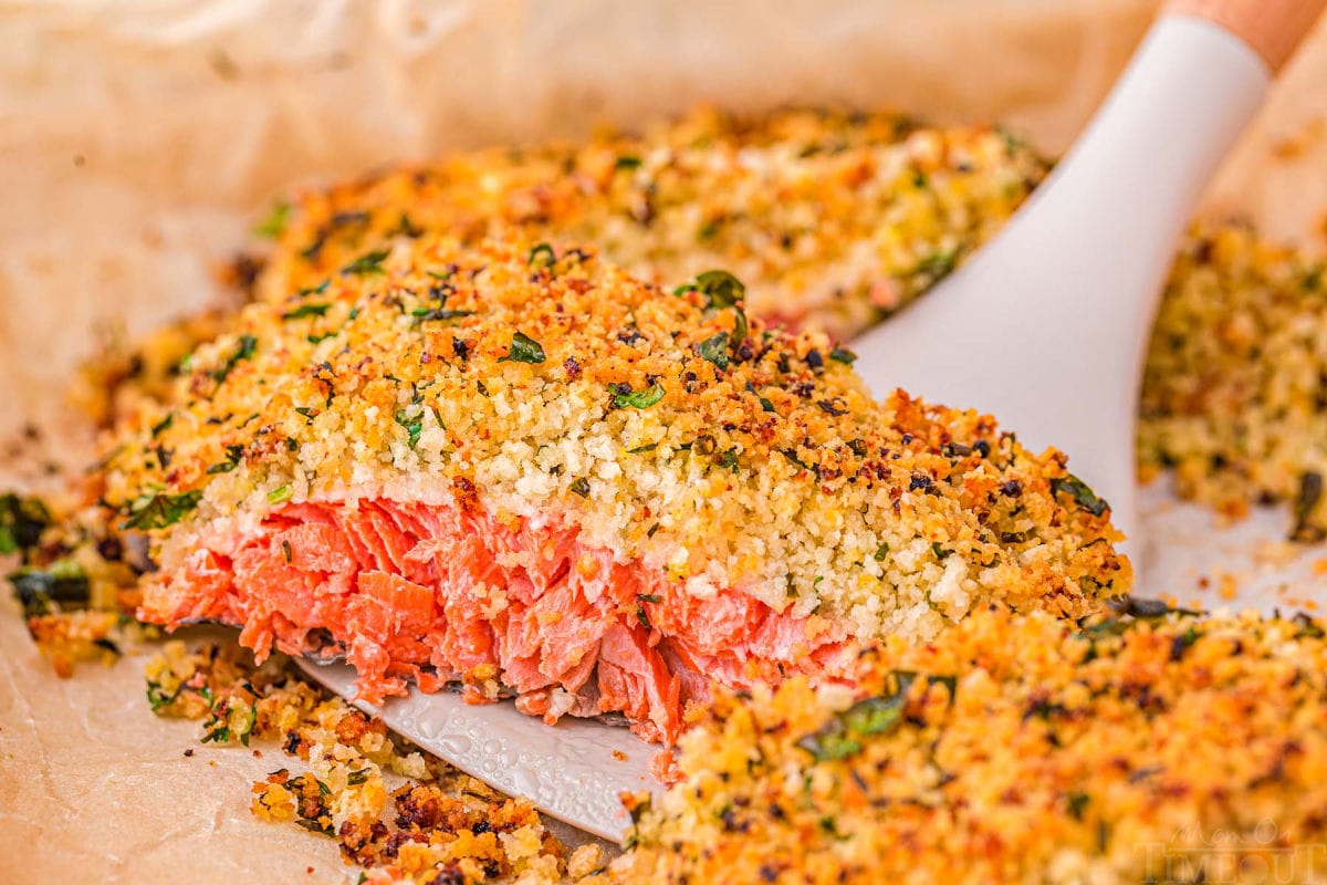 piece of salmon being lifted off a parchment lined sheet tray with a spatula.