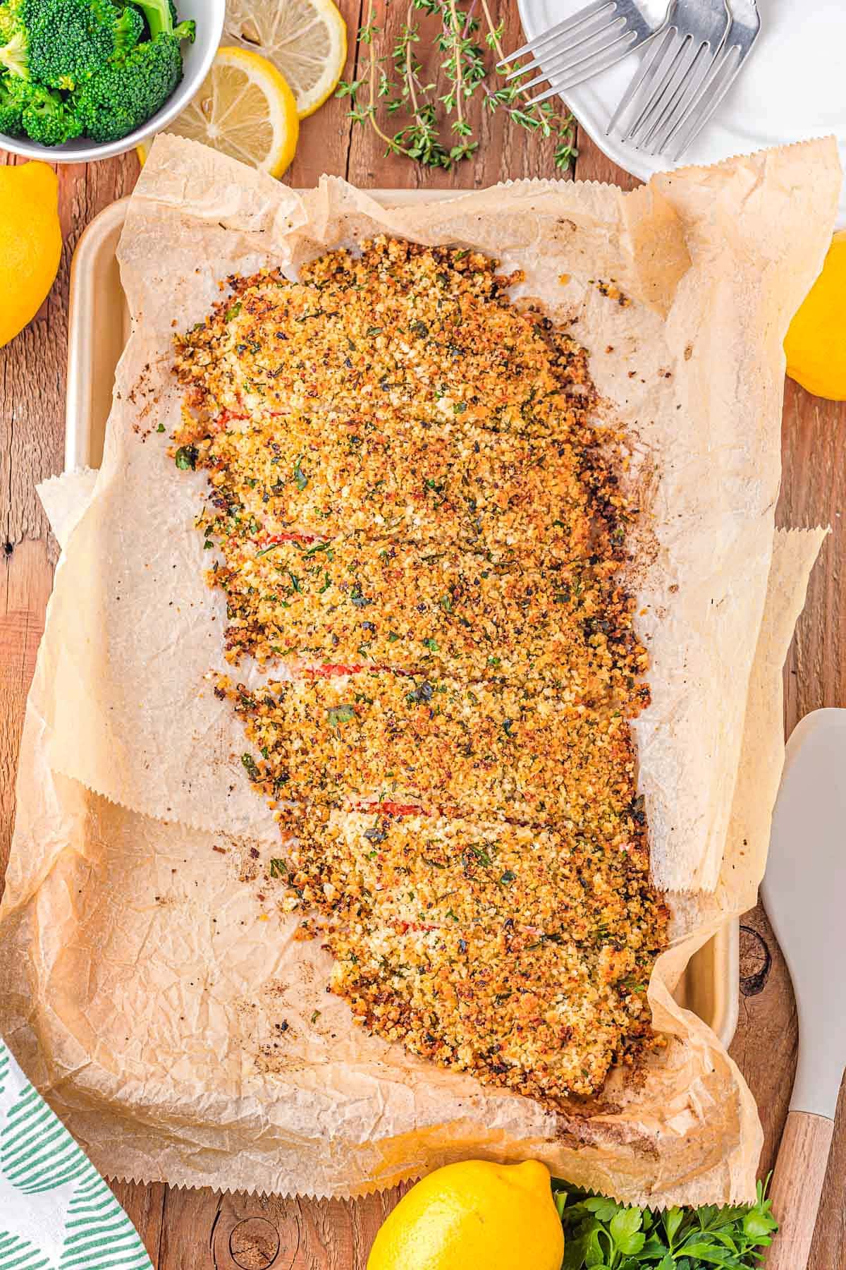 top down view of a bake salmon filet with a crust made with parmesan, panko and herbs. the filet is sitting on a parchment lined baking sheet.