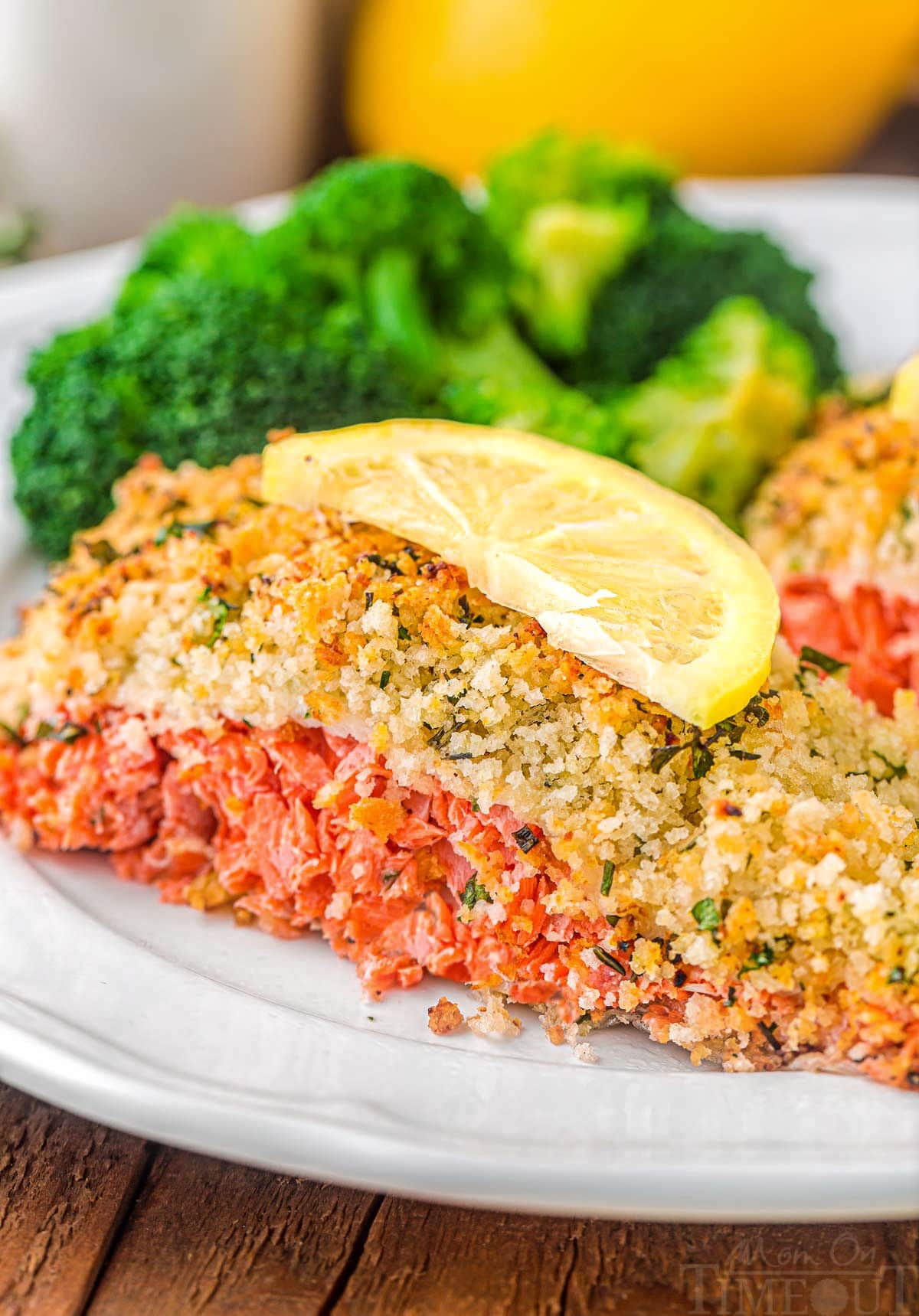 piece of salmon with a panko crust sitting on a plate with broccoli and a slice of lemon on top of it.