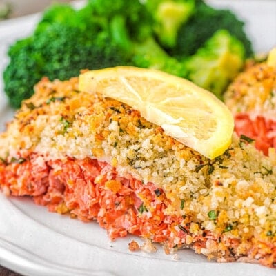 piece of salmon with a panko crust sitting on a plate with broccoli and a slice of lemon on top of it.