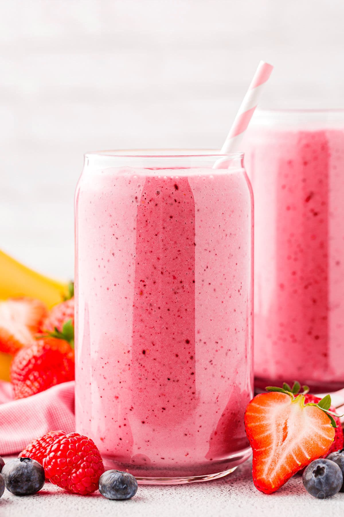 head on shot of two glasses with bright pink smoothies and scattered berries around the base of the glasses.