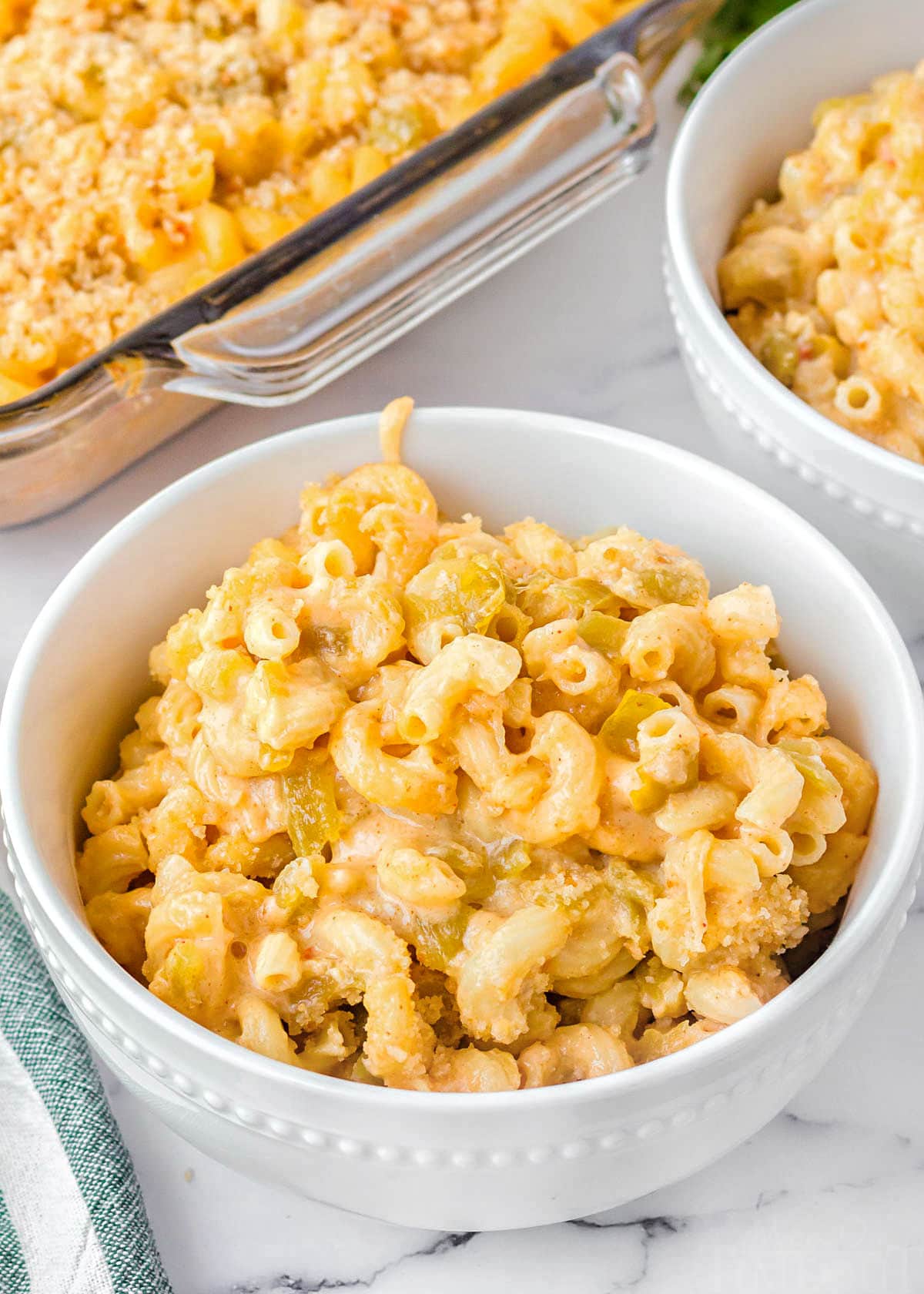 mac and cheese in a white bowl sitting on a marble surface. casserole dish and another bowl can be seen in the background.