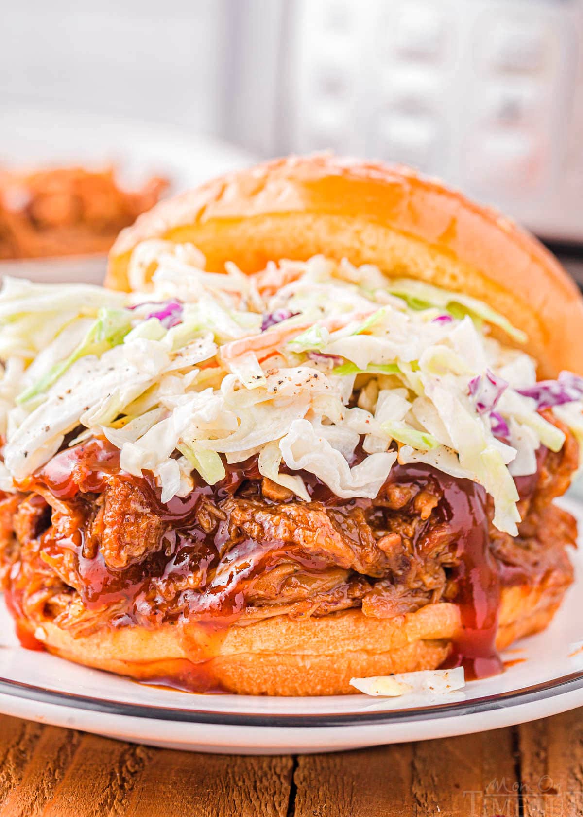 pulled pork sandwich topped with coleslaw on a white plate with instant pot in the background.