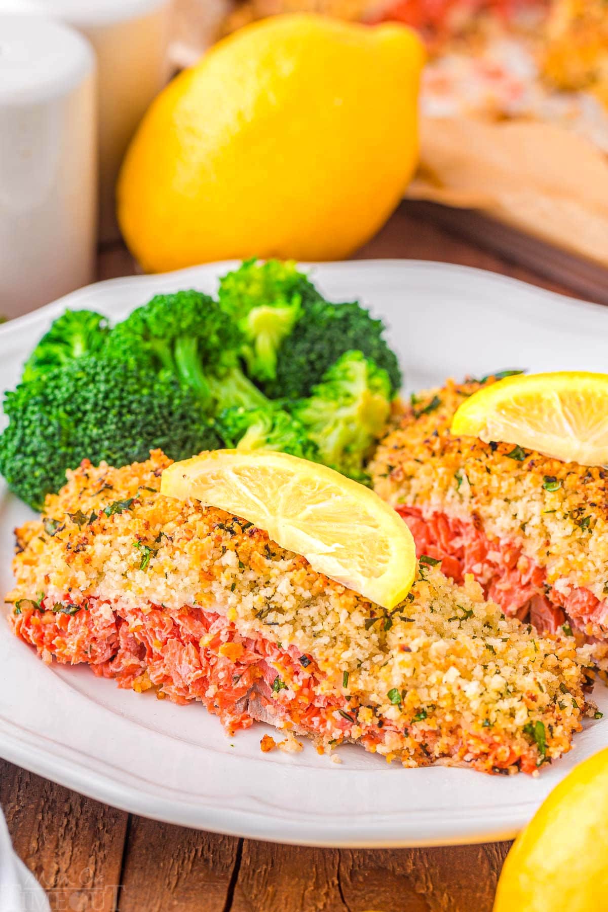 two pieces of salmon with a panko crust sitting on a plate with broccoli and a slice of lemon on top of each filet.