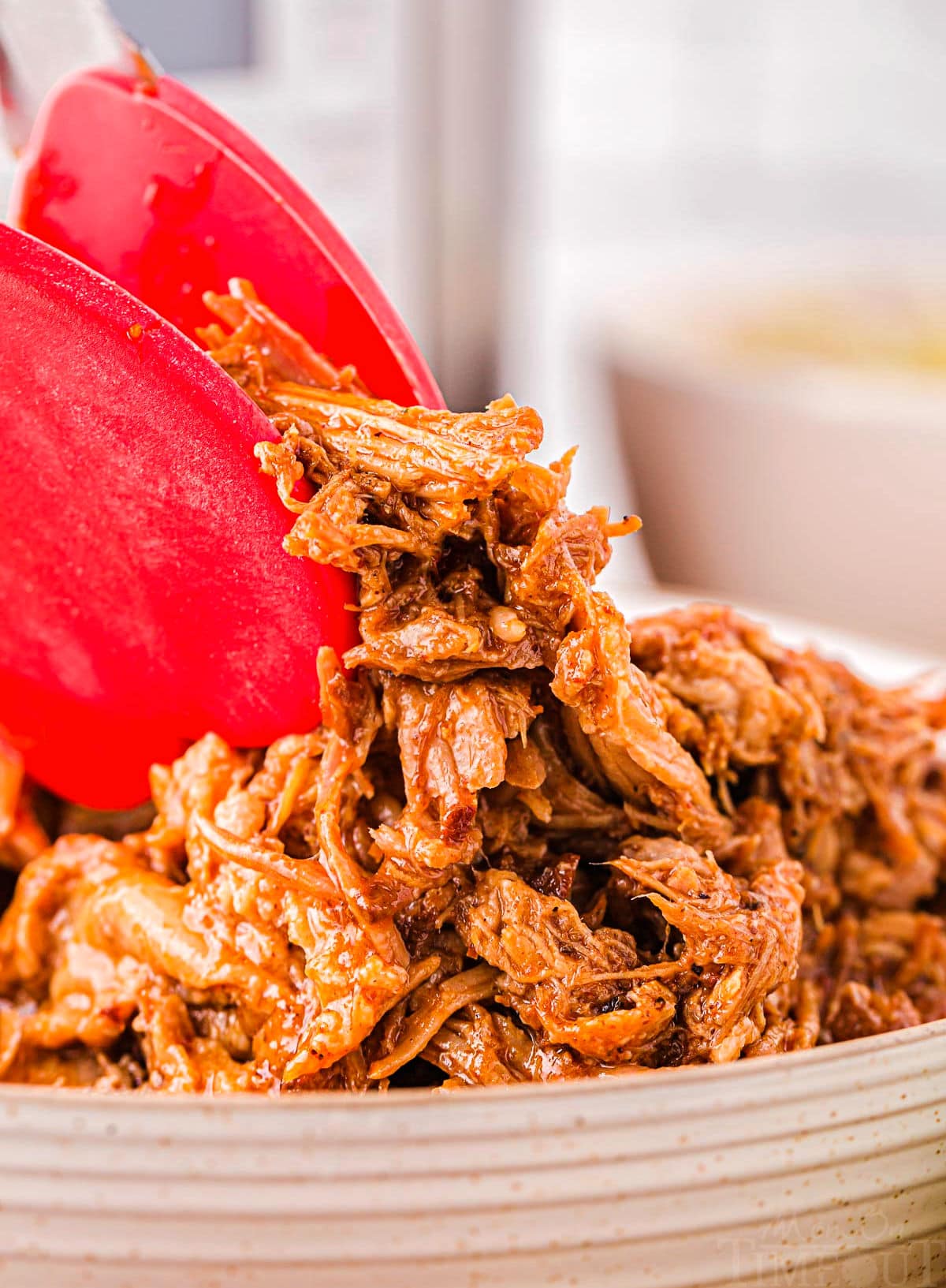 pair of red tongs holding up shredded pulled pork made in the instant pot.