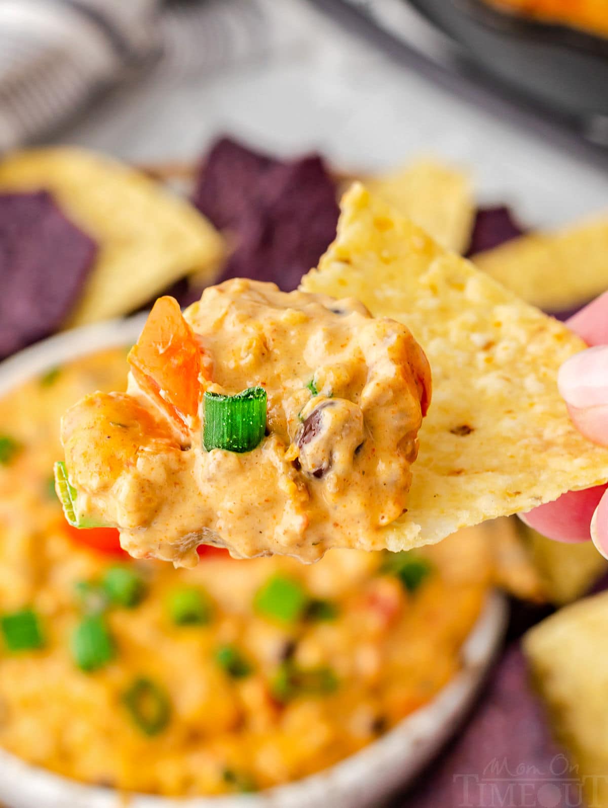 rotel dip scooped onto a tortilla chip held over a bowl of the dip.