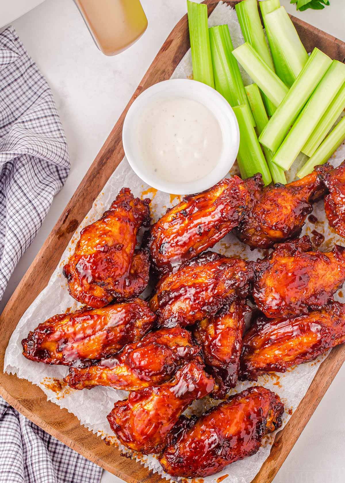 top down look at bbq chicken wings on wood board with celery sticks and ranch.