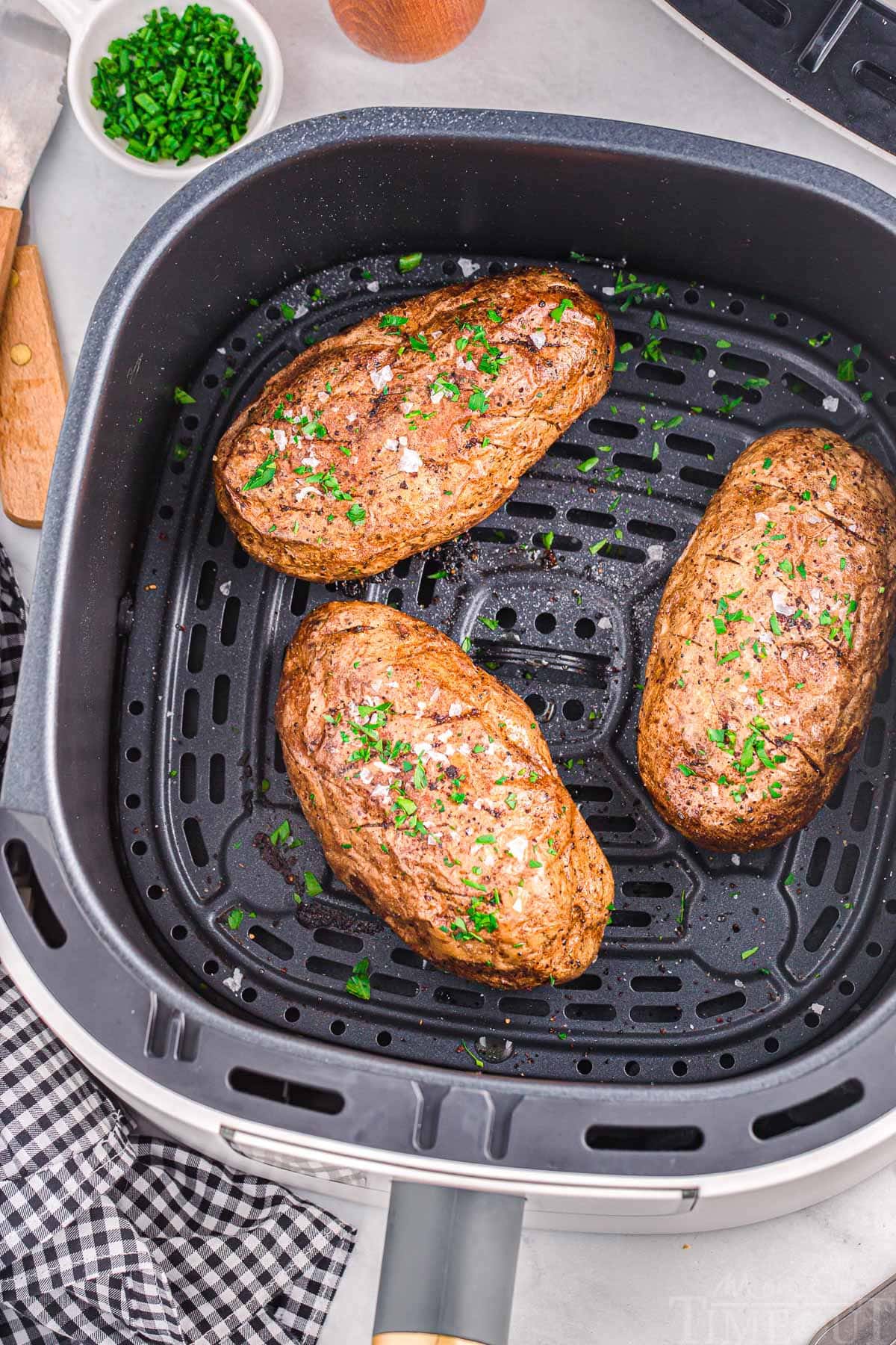 top down view of three potatoes in an air fryer basket.