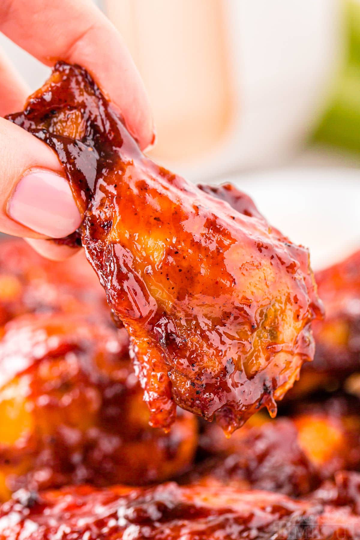 hand holding a chicken wing made in the air fryer and brushed with barbecue sauce.