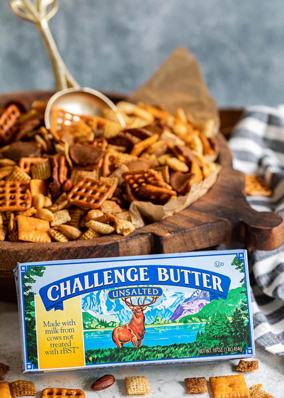 challenge butter box sitting in front of large wood bowl of chex mix with a gold scoop sticking out of it.