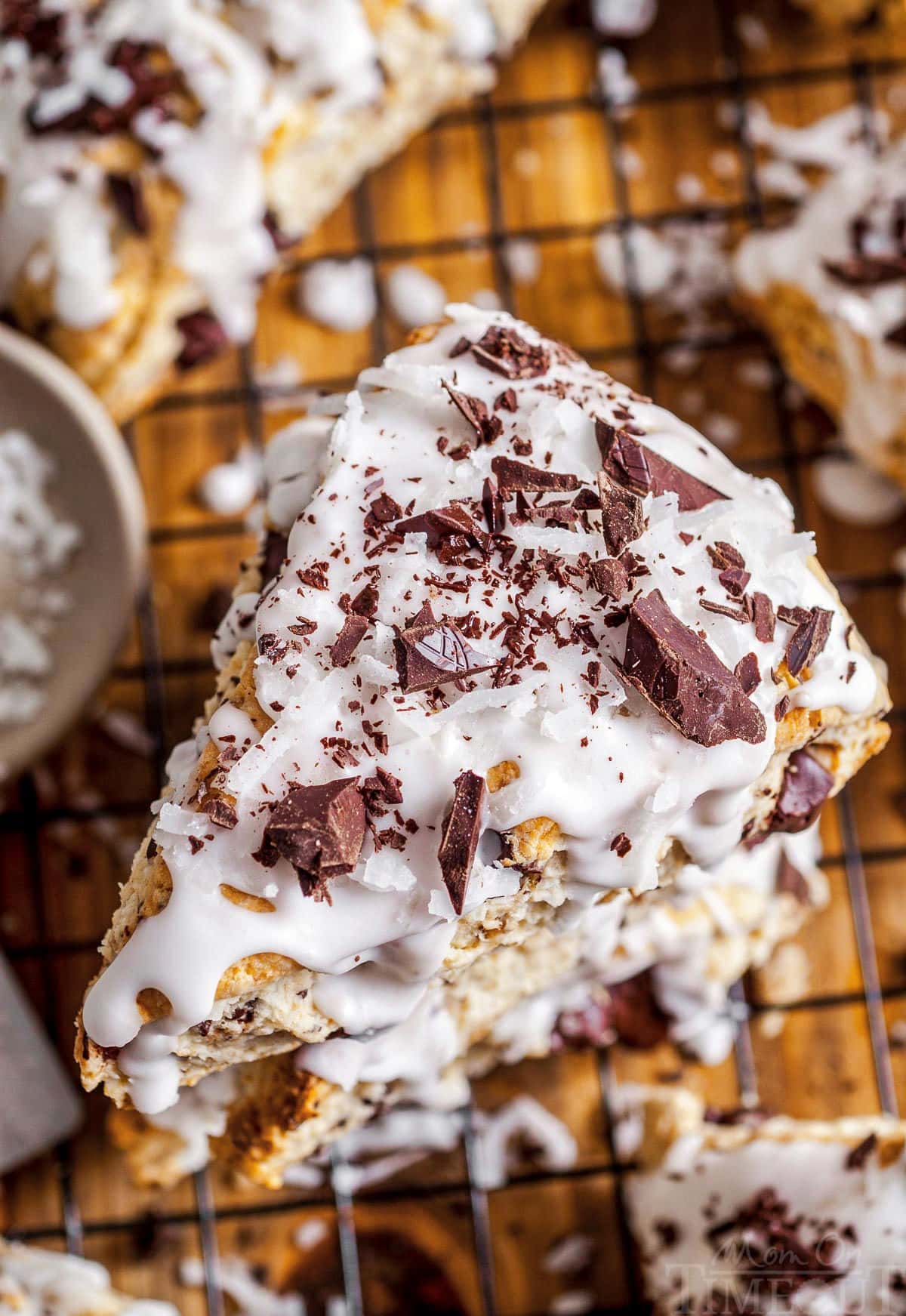 top down view of three coconuts scones stacked on top of each other and topped with coconut icing and chocolate shavings.