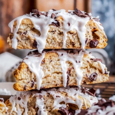 three almond joy scones stacked on a wood board.