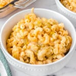 mac and cheese in a white bowl sitting on a marble surface. casserole dish and another bowl can be seen in the background.