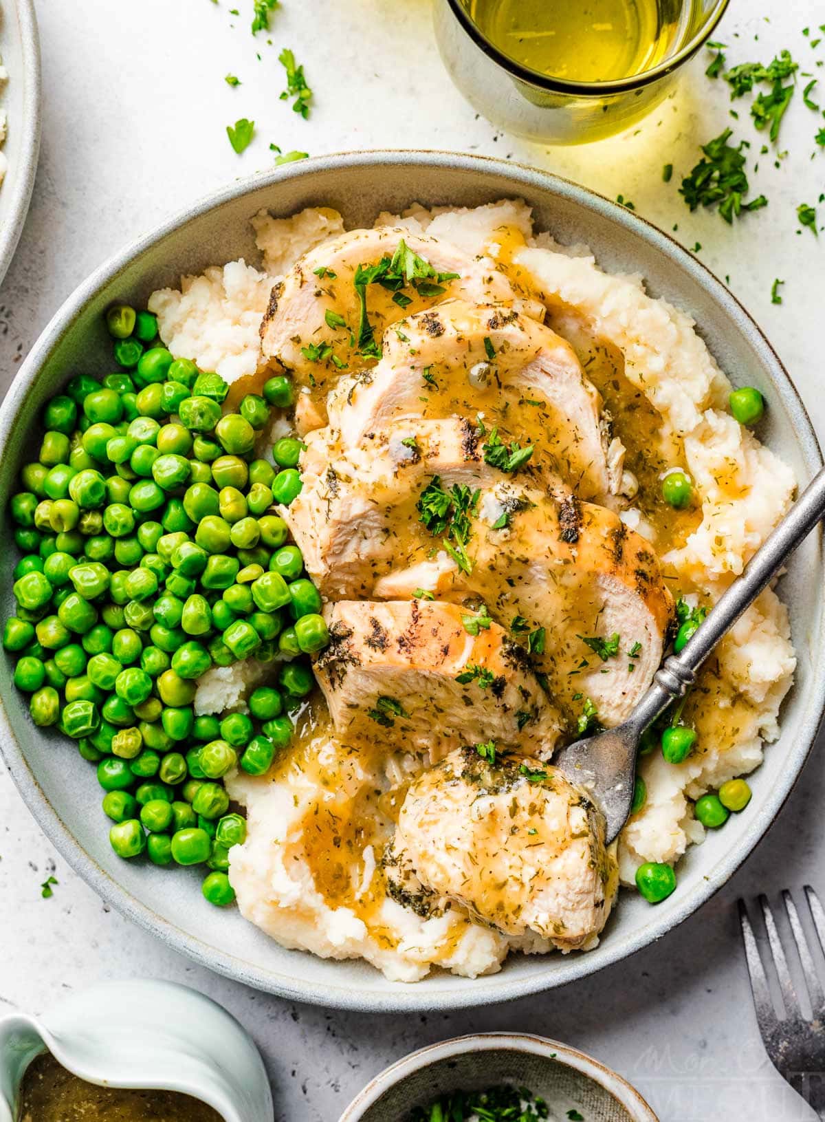 top down look at instant pot chicken breast sliced sitting on a bed of mashed potatoes with gravy over the top. green peas are also on the plate.