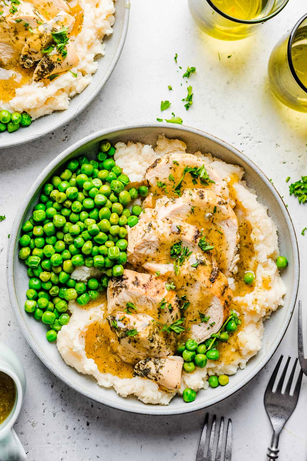 top down look at instant pot chicken breast sliced sitting on a bed of mashed potatoes with gravy over the top. green peas are also on the plate.