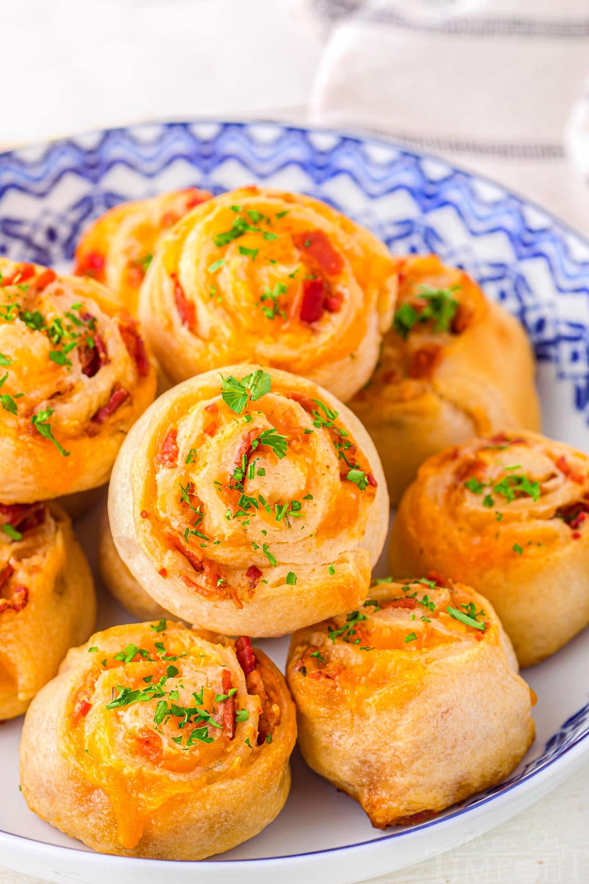 pinwheels appetizer made with crescent dough, cheese and bacon stacked in a blue and white bowl ready to be enjoyed.