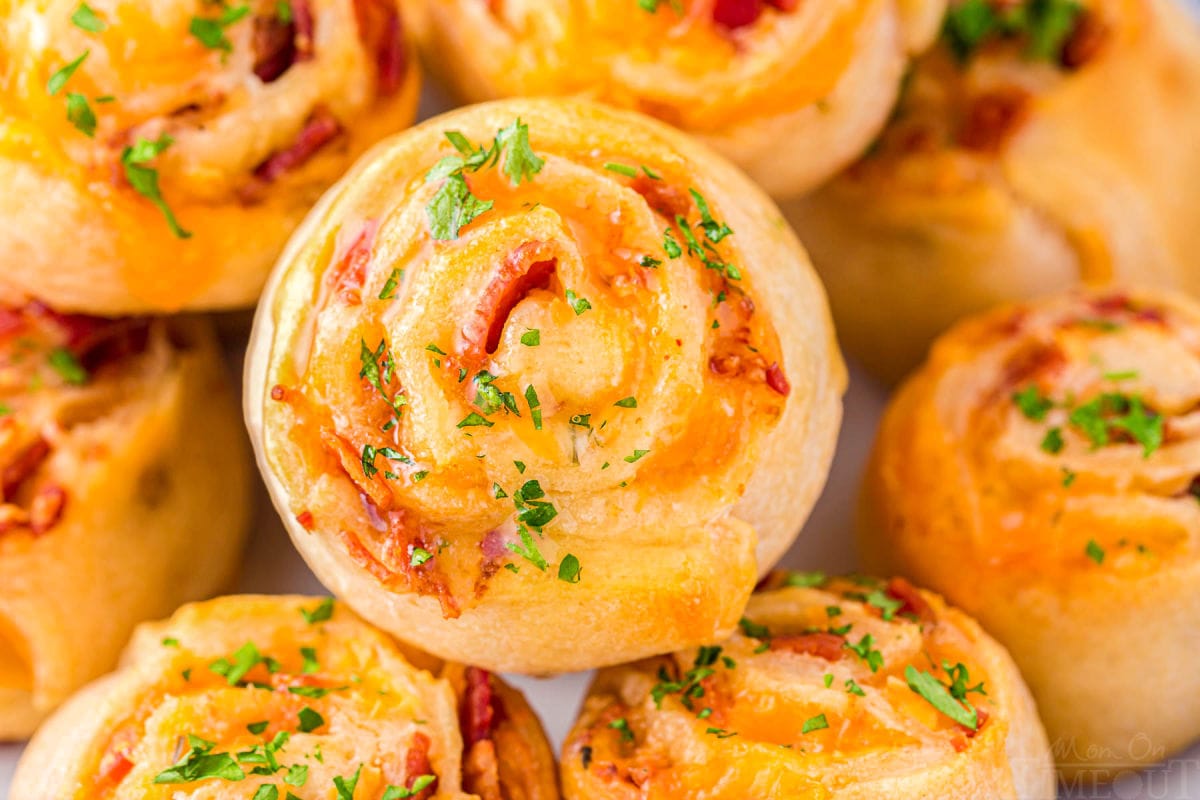 pinwheels recipe made with bacon and cheddar stacked on a plate and topped with freshly chopped parsley.