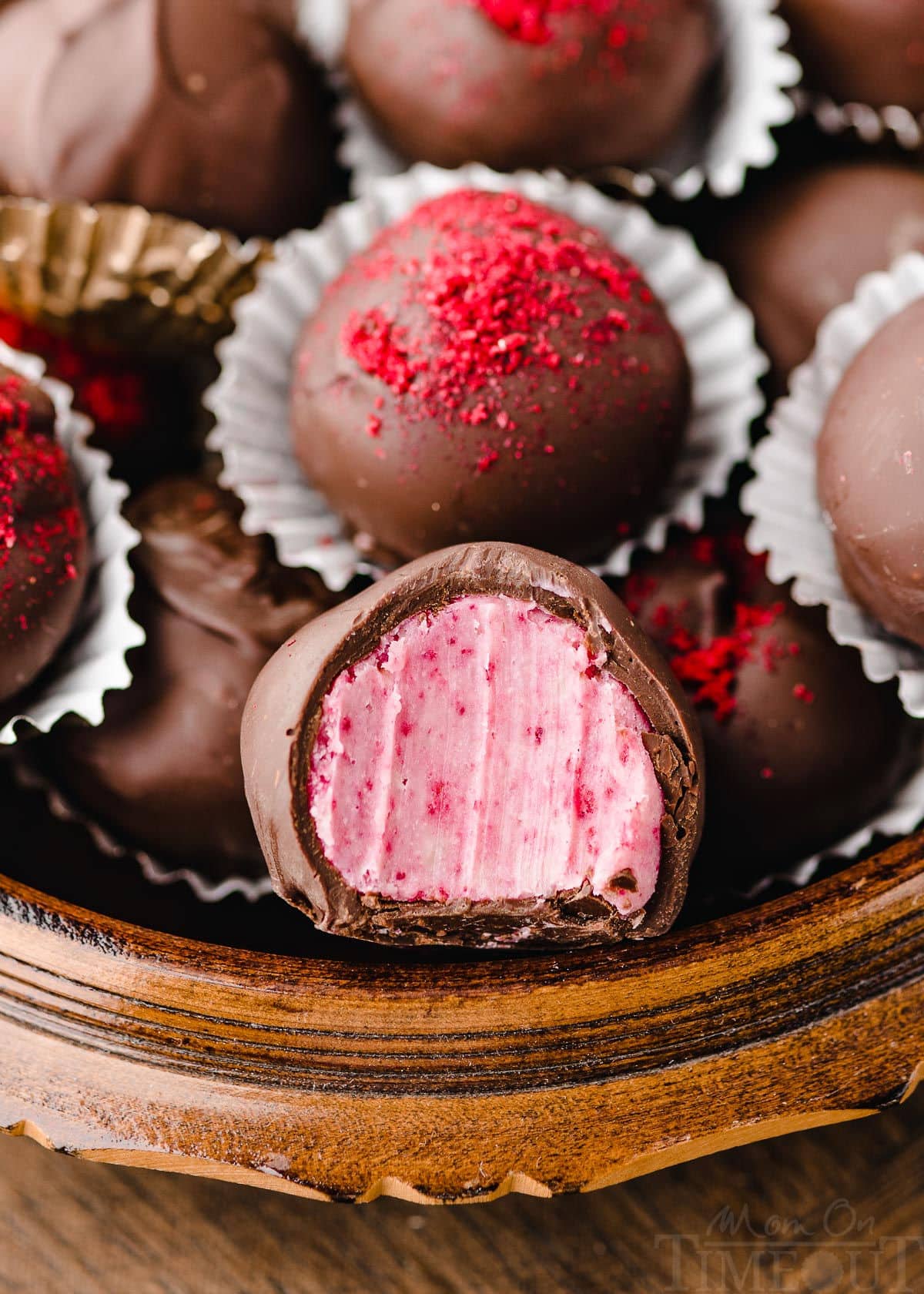 round wooden box filled with raspberry truffles. front truffle has a bite taken out of it. some of the truffles are topped with freeze dried raspberry dust.