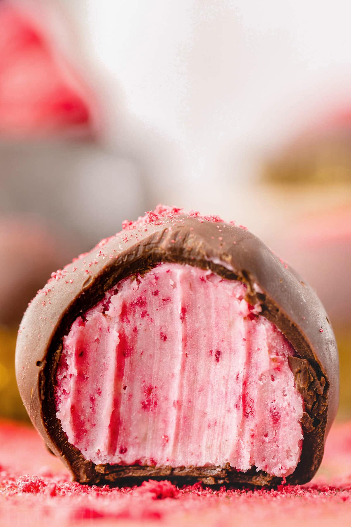 close up look at a single raspberry truffle with a bite taken out of it so you can see the creamy raspberry interior.