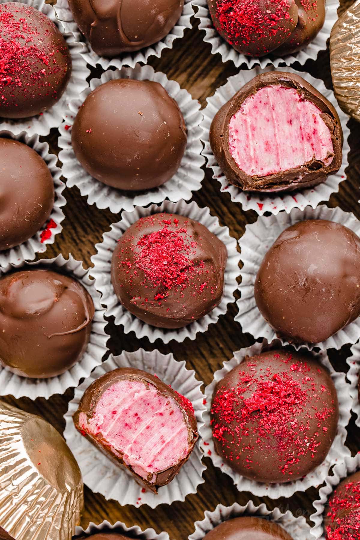 top down look at a dozen or so raspberry chocolate covered truffles in a wooden box. two of the truffles have been bitten in half.