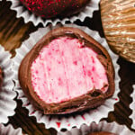 close up of a raspberry truffle covered in dark chocolate in small paper liners next to more truffles.