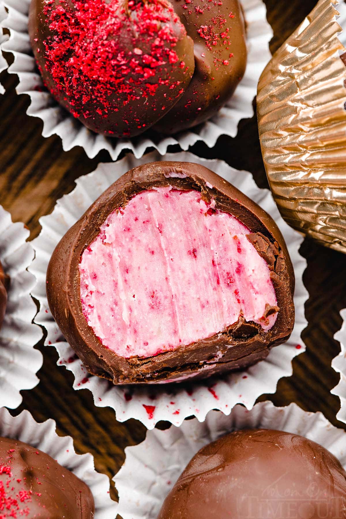 close up of a raspberry truffle covered in dark chocolate in small paper liners next to more truffles.