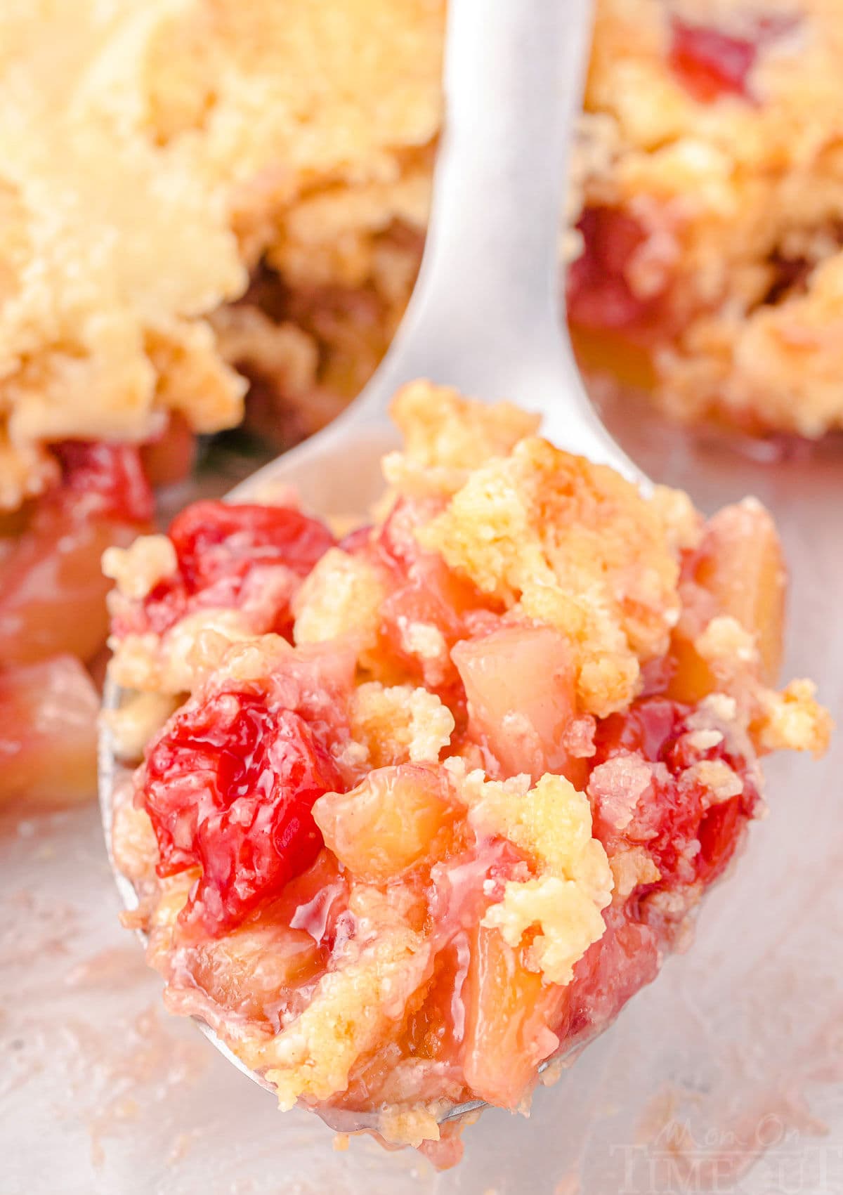 serving spoon filled with a scoop of dump cake made with cherry pie filling and pineapple resting just above the baking dish.