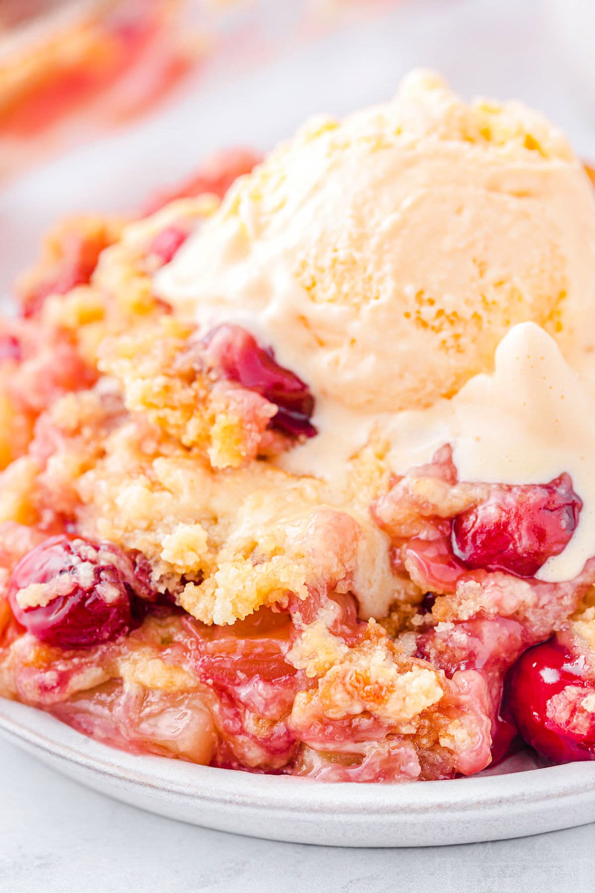 plate filled with cherry pineapple dump cake and topped with a scoop of vanilla ice cream that is just beginning to melt. cherries and pineapple chunks are visible in the cake.