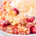 plate filled with cherry pineapple dump cake and topped with a scoop of vanilla ice cream that is just beginning to melt. cherries and pineapple chunks are visible in the cake.