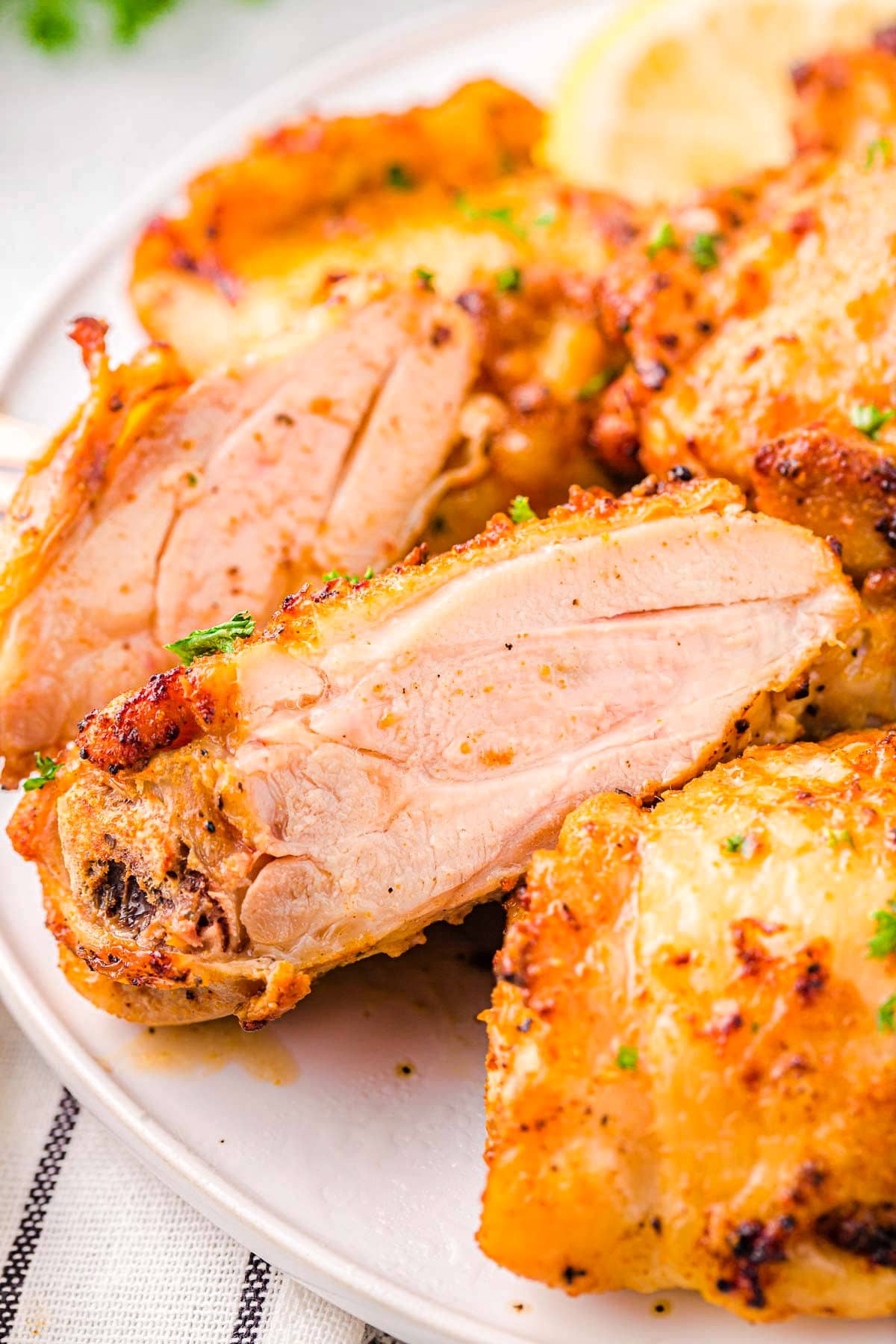 chicken thighs made in the air fryer on a white plate. One chicken thigh is cut in half so you can see the juicy meat.