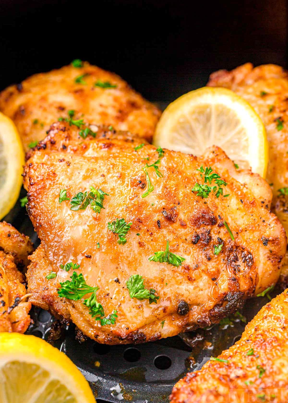 chicken thigh in air fryer cooked until golden brown, topped with parsley and lemon slices.