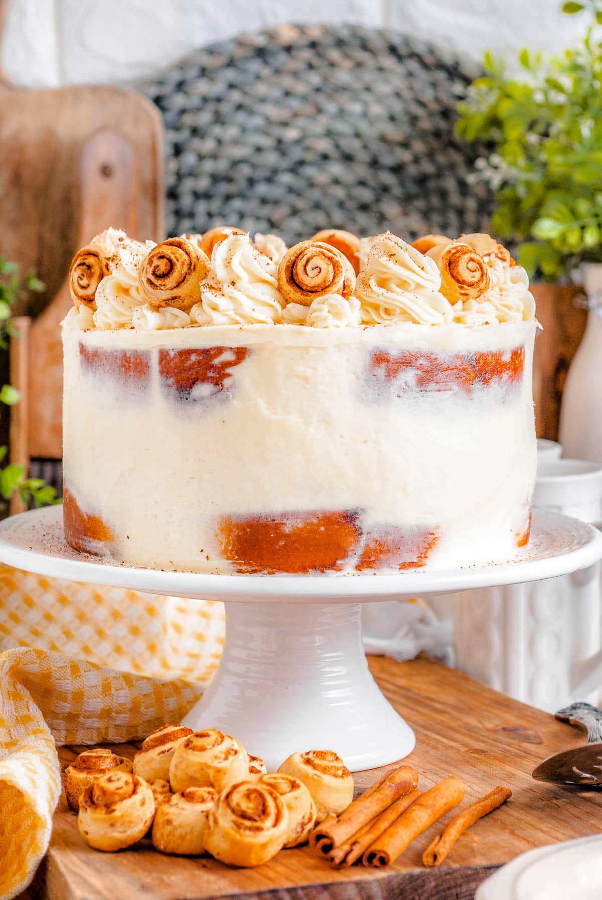 cake made with cinnamon rolls on a white cake stand and topped with cream cheese frosting and mini cinnamon rolls.