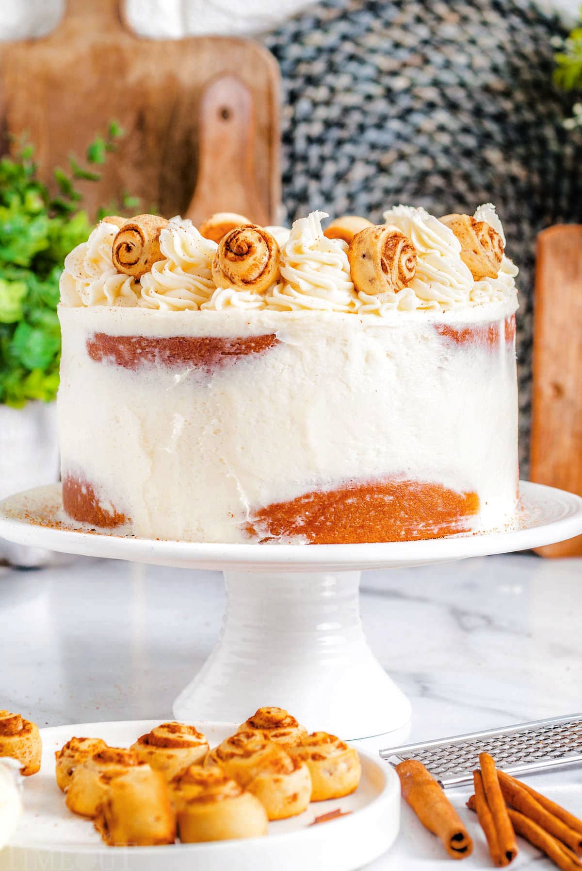 cake made with cinnamon rolls on a white cake stand and topped with cream cheese frosting and mini cinnamon rolls.