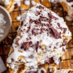 top down view of three coconuts scones stacked on top of each other and topped with coconut icing and chocolate shavings.