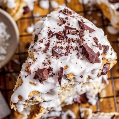 top down view of three coconuts scones stacked on top of each other and topped with coconut icing and chocolate shavings.